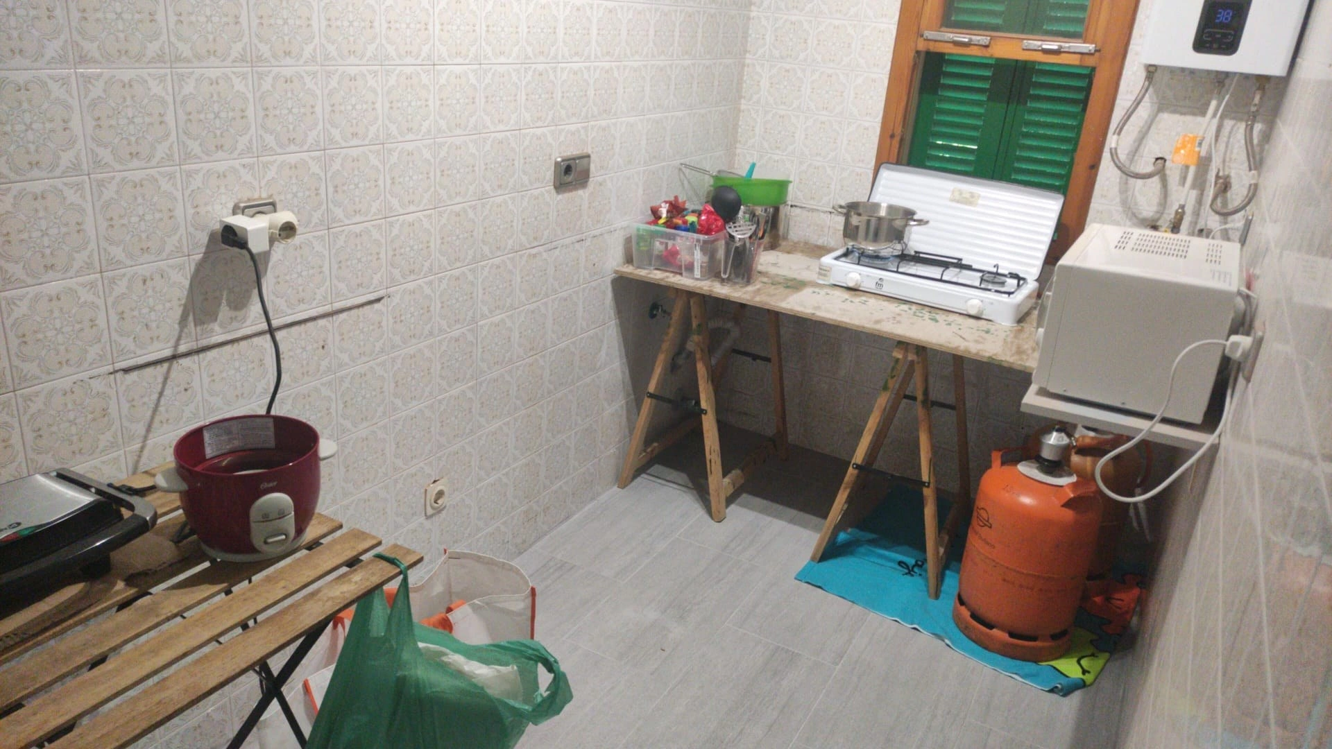 Cocina vacía tras desmontar la anterior, con una cocina de emergencia: mesa de caballete, hornillo, bombona de butano y microondas, y el alicatado original en la pared