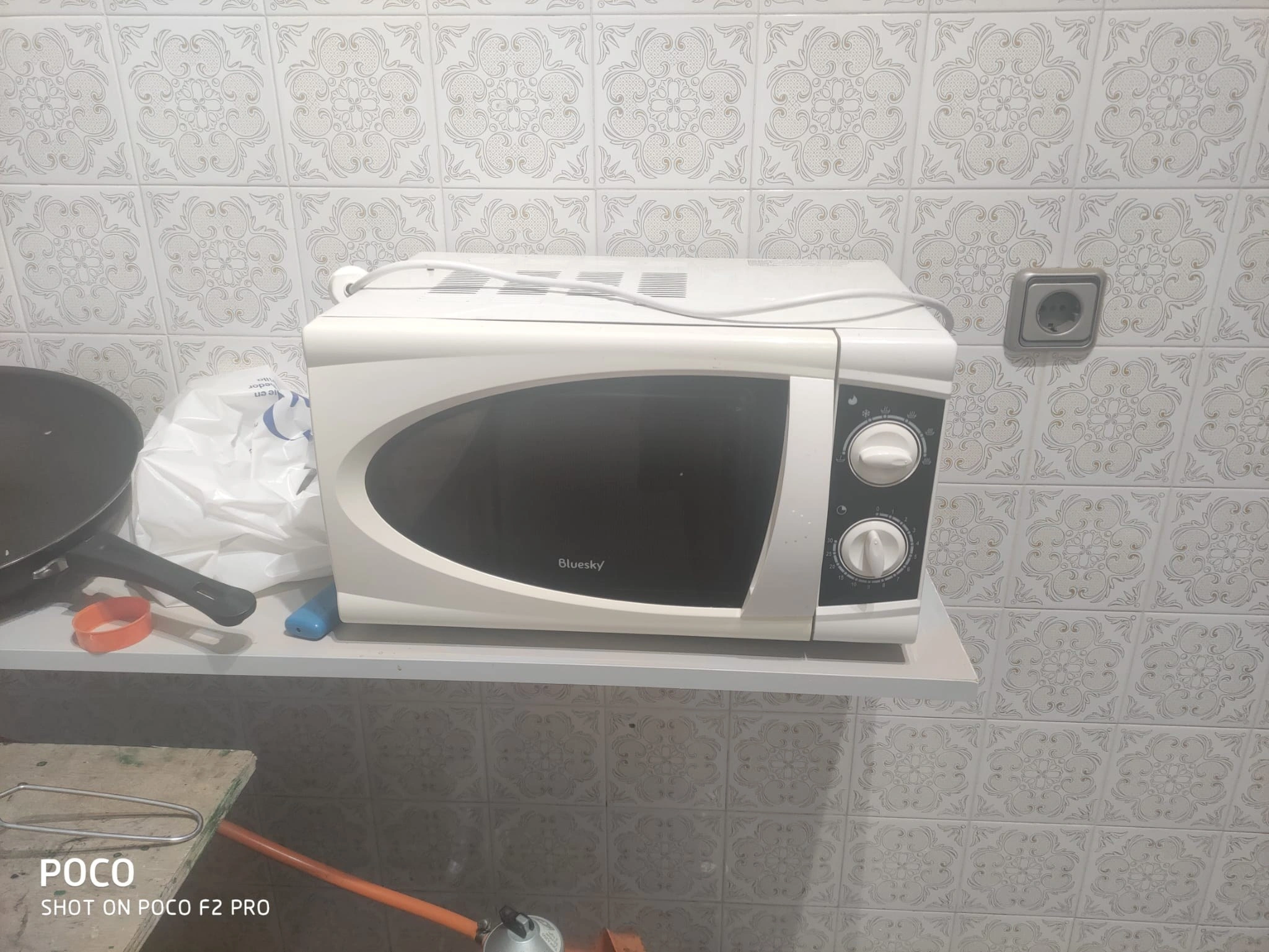 Microondas apoyado en una balda sobre el alicatado original, en la zona de paso de la cocina, antes de la reforma
