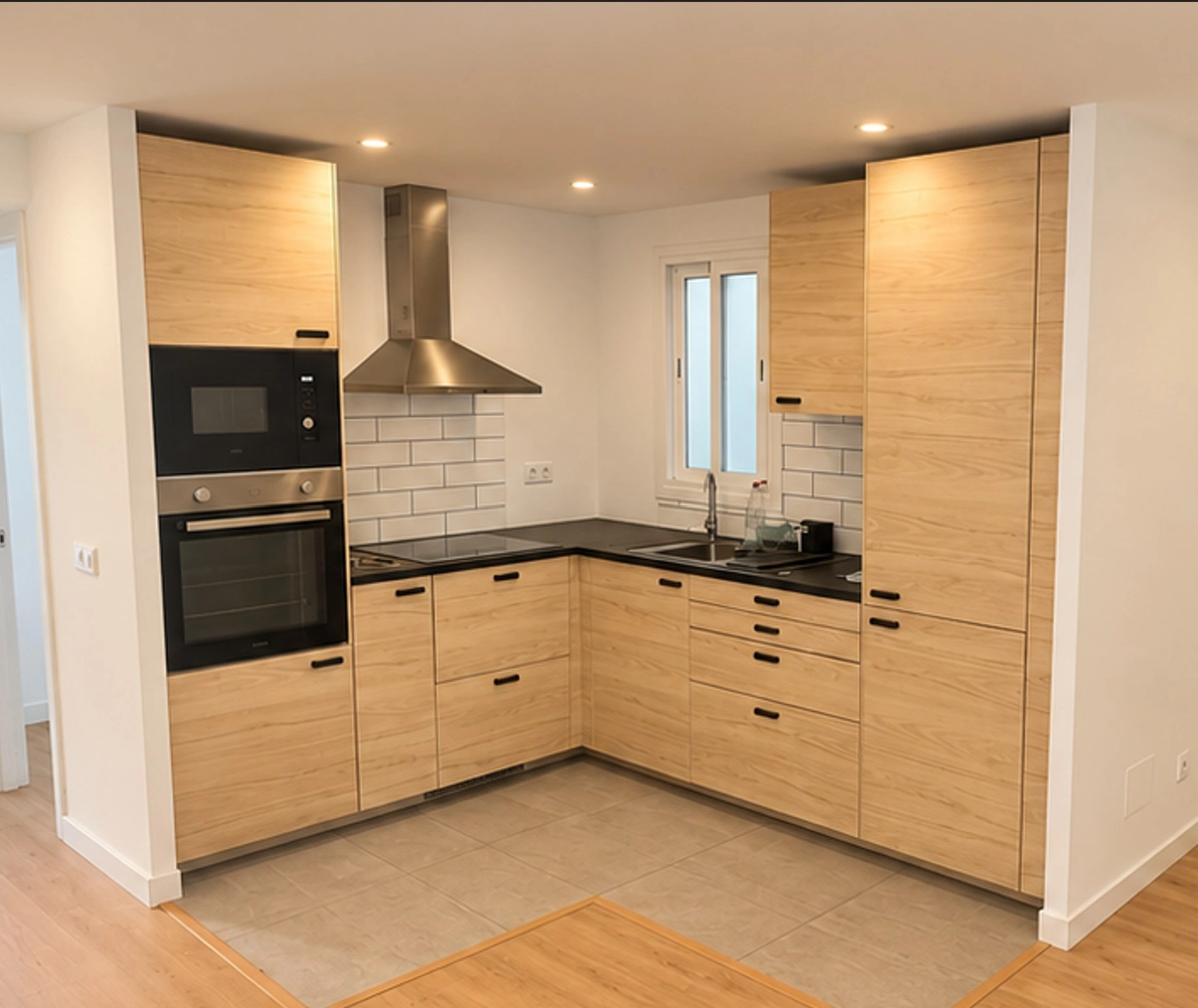 Cocina abierta antes de la reforma en un piso de Mallorca: distribución en L con el centro vacío, muebles sin cerrar a techo, campana convencional y el suelo del baño bajo los muebles