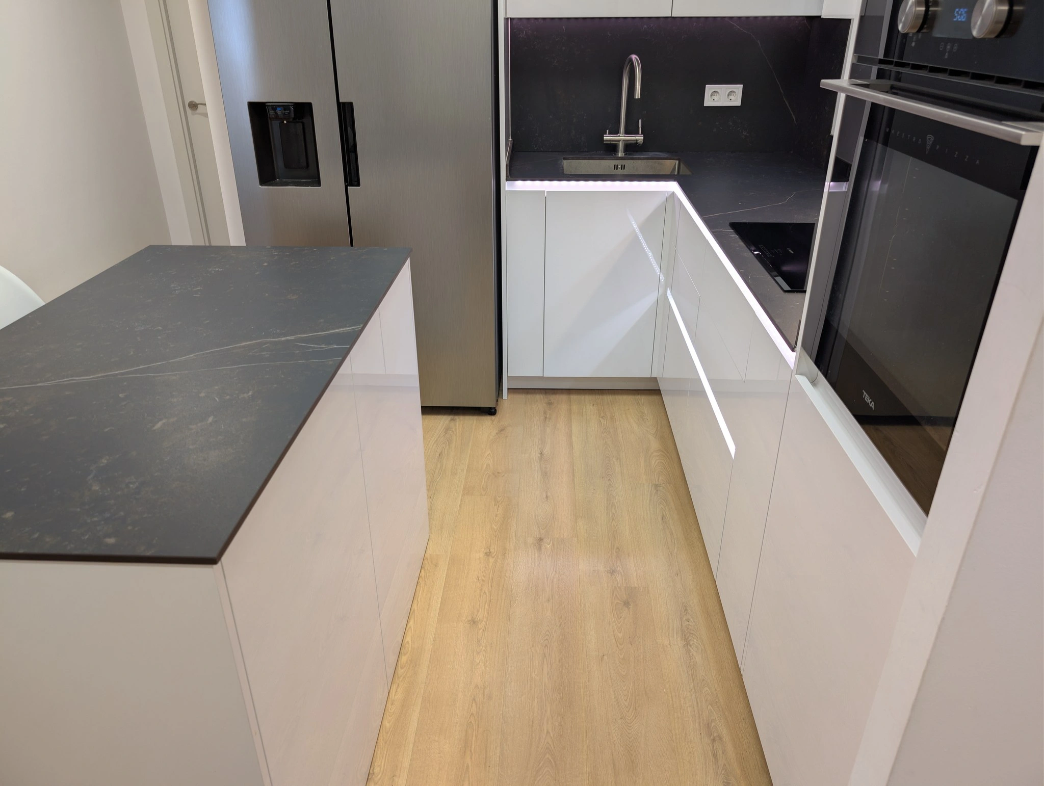 Detalle de la encimera de Dekton de la isla y el paso libre entre la isla y la línea de muebles con la luz LED en los tiradores gola