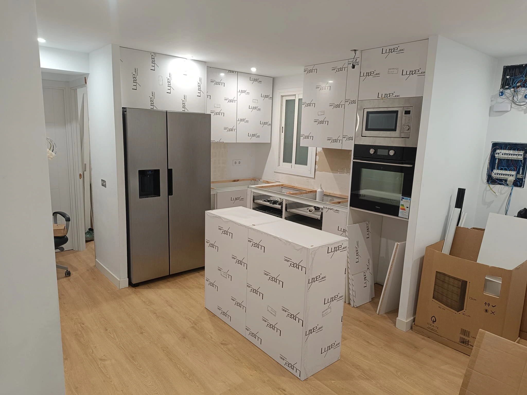 Cocina en obra con la isla ya montada y protegida, y los muebles altos cerrando hasta el techo con las puertas fabricadas a partir de costados de columna