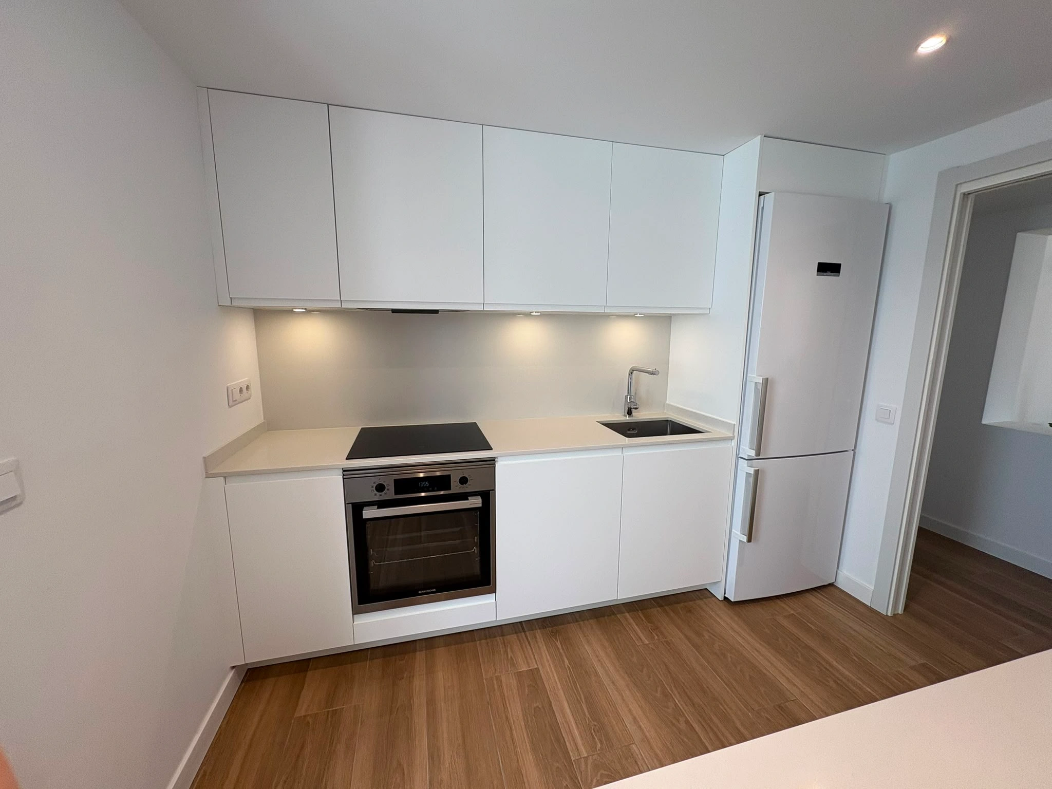 Renovated kitchen in Palma with white cabinets up to the ceiling, hob with oven integrated underneath, sink and fridge integrated into the run