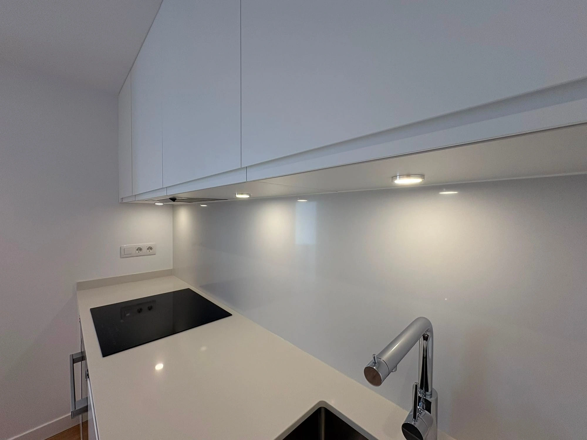 Detail of the white porcelain worktop and the spotlights integrated under the cabinets that light the work area