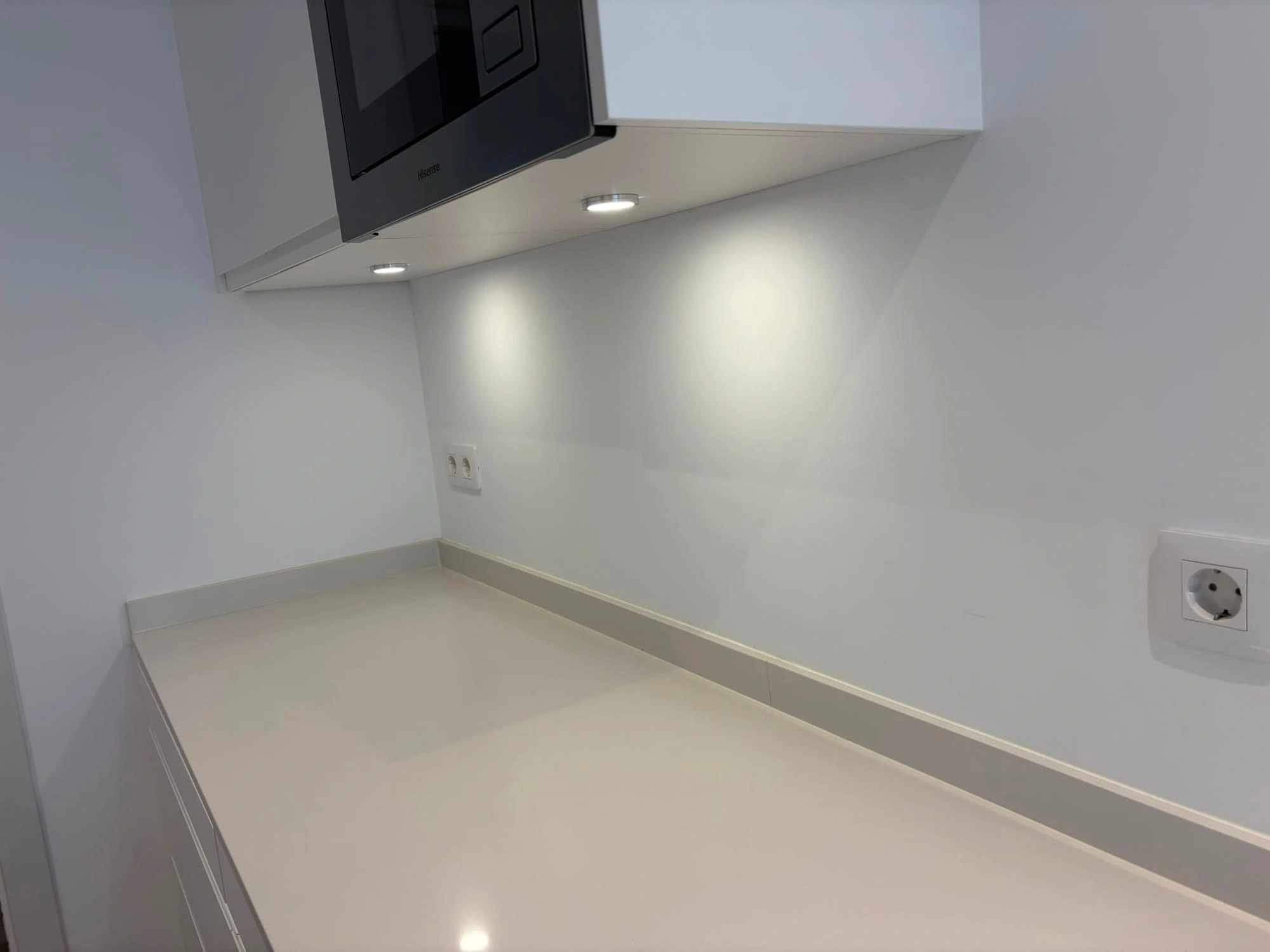 Microwave built into a tall kitchen unit, with the spotlights integrated under the cabinets switched on
